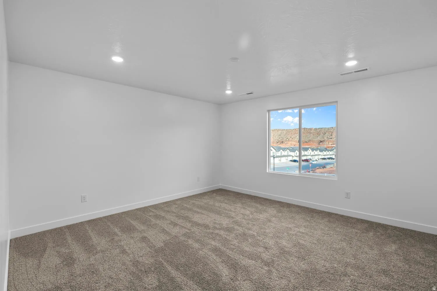 Recessed lighting throughout, neutral carpeting, expansive window, and crisp white walls