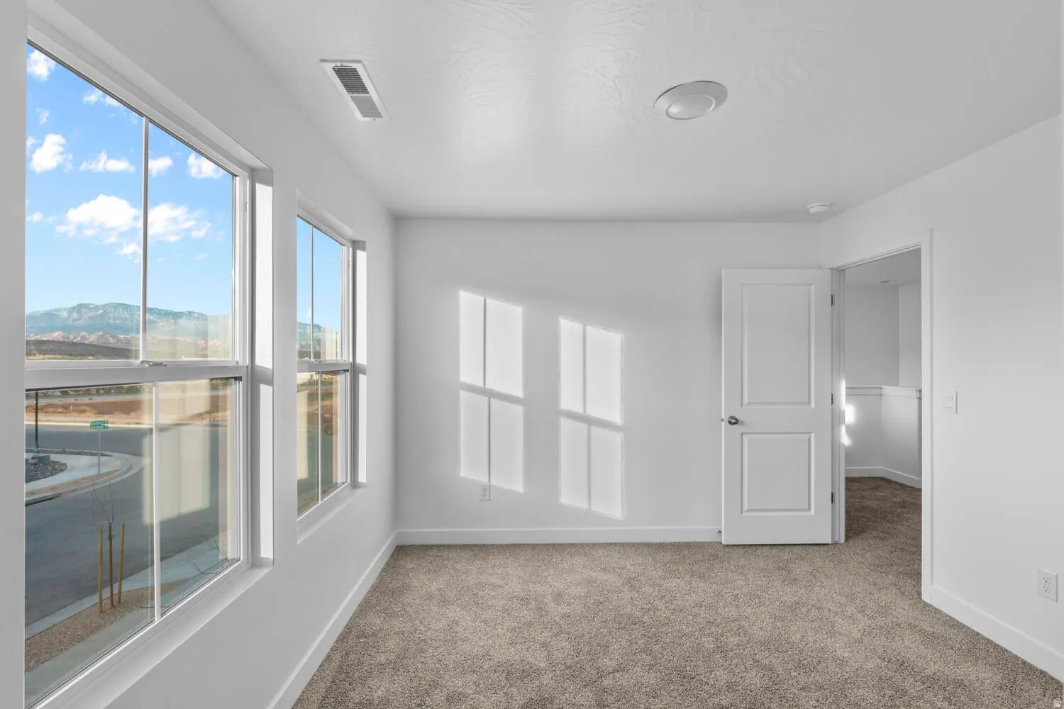 Bright interior with neutral carpet flooring, white walls, and a white paneled door