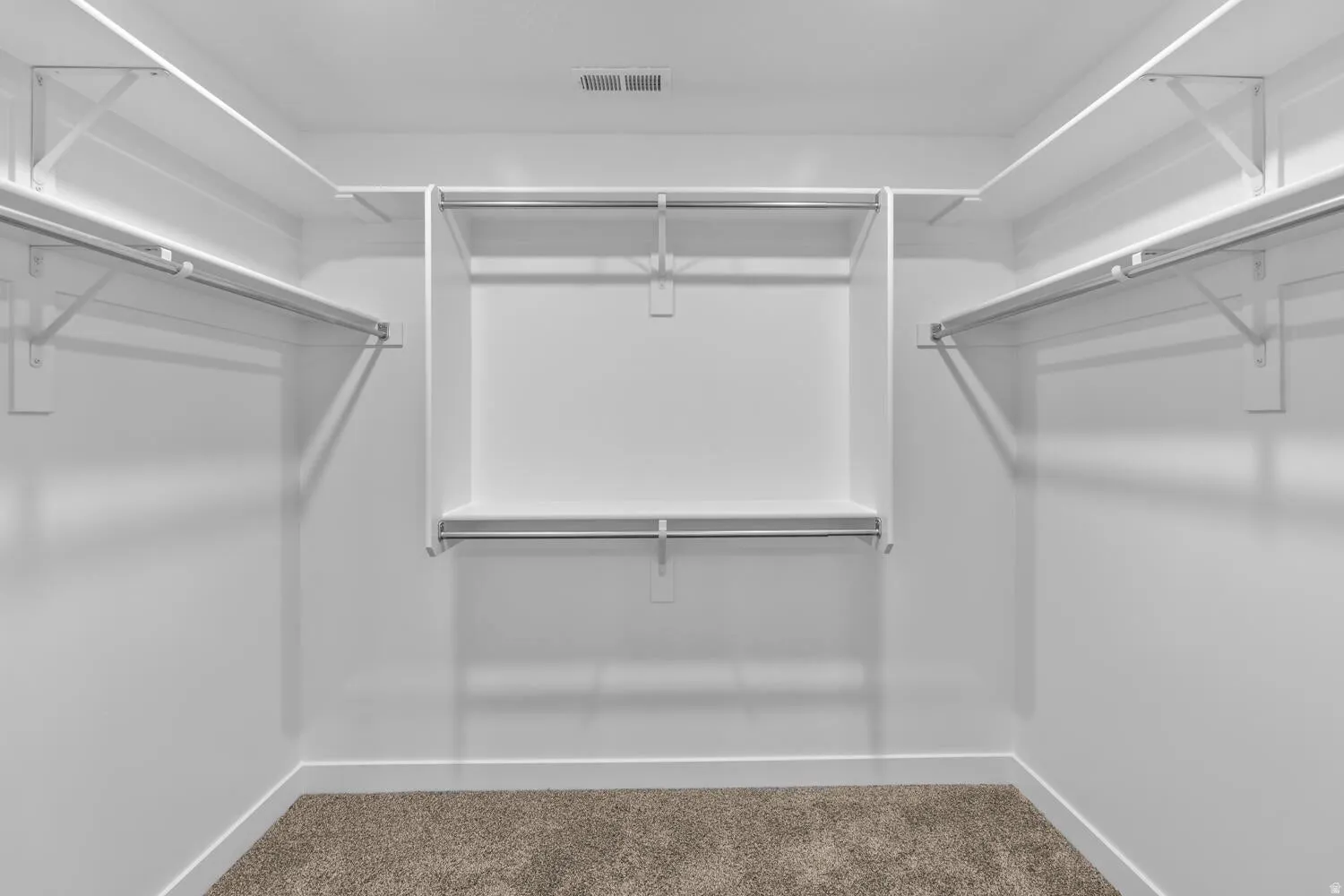 Spacious walk-in closet with multiple hanging rods, integrated shelving, and neutral carpeting