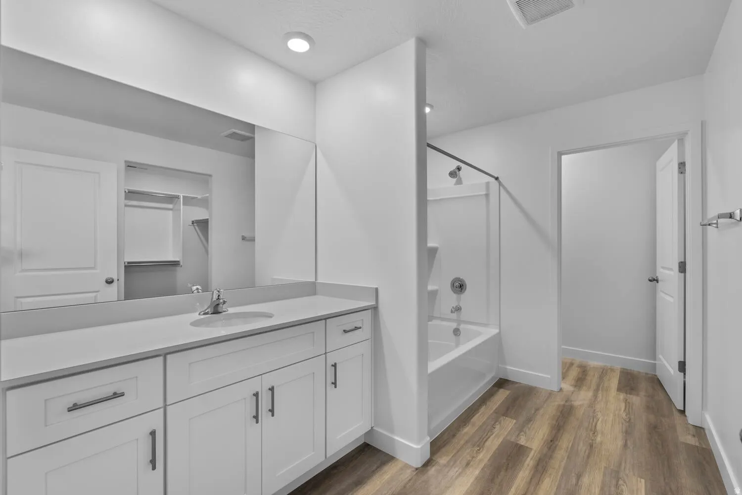 White vanity with multiple cabinets and drawers, an integrated sink, and an expansive wall mirror
