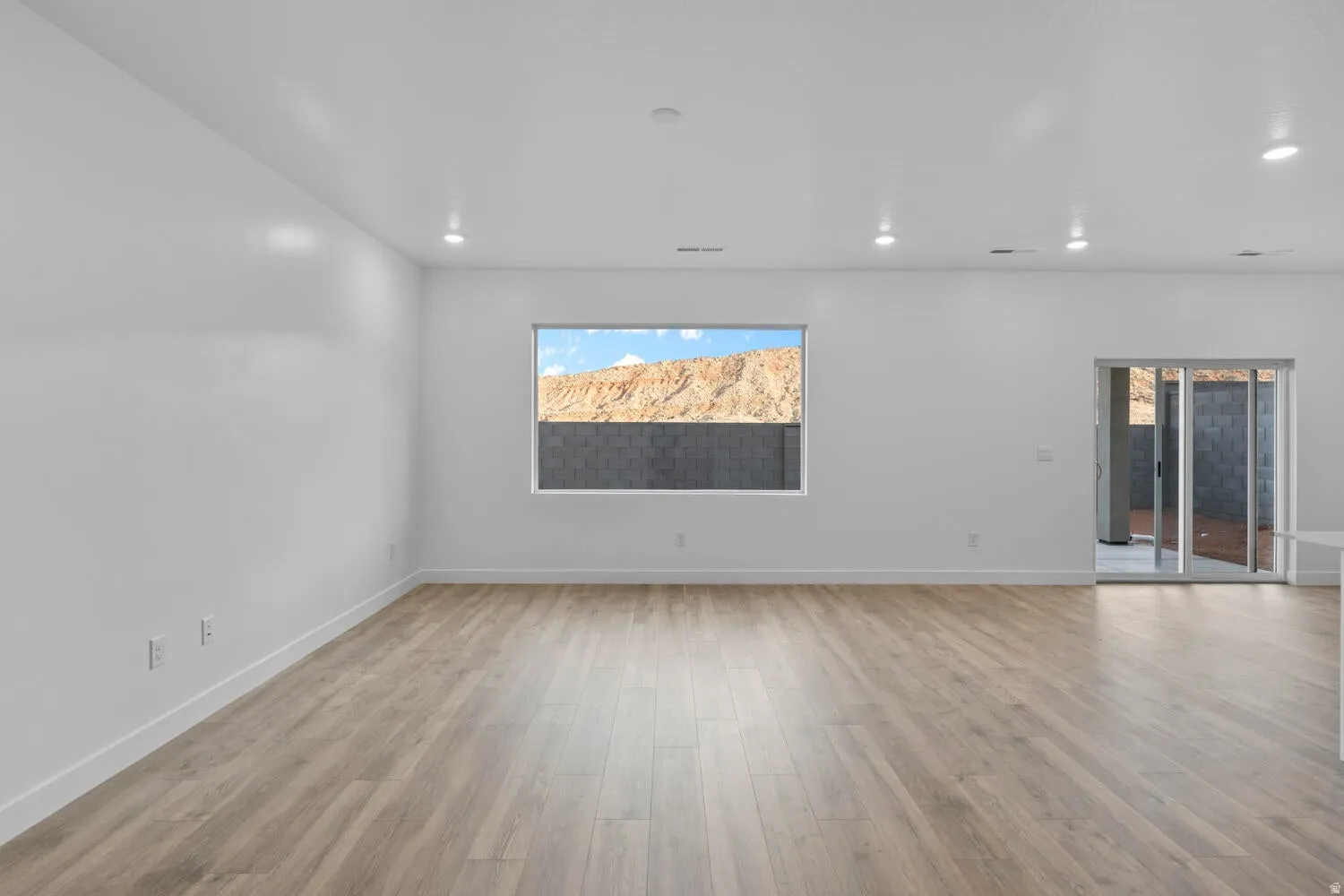 Spacious interior with light wood-finish flooring, recessed lighting, and a large window offering a mountain backdrop