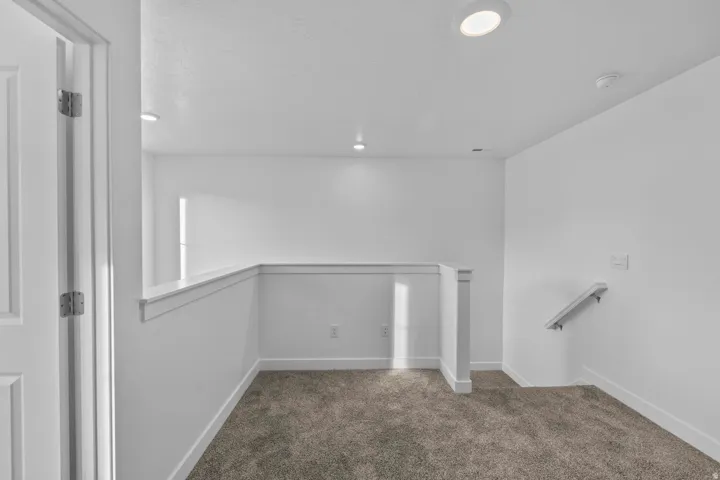 Carpeted landing featuring white walls, recessed ceiling lights, and a white handrail