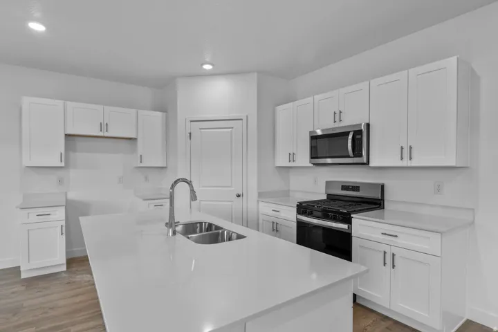 Kitchen featuring white shaker cabinetry, stainless steel appliances, a center island with a double basin sink, and wood-finish flooring