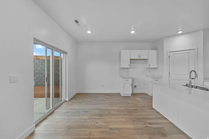 Open-concept living space with wood-finish flooring, white cabinetry, recessed lighting, and a kitchen island with an undermount sink and gooseneck faucet