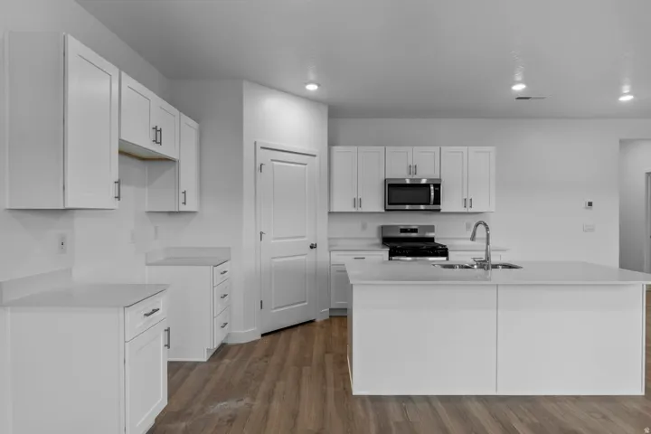 Kitchen featuring white shaker-style cabinetry, stainless steel appliances, a large center island with an undermount sink, recessed lighting, and wood-finish flooring