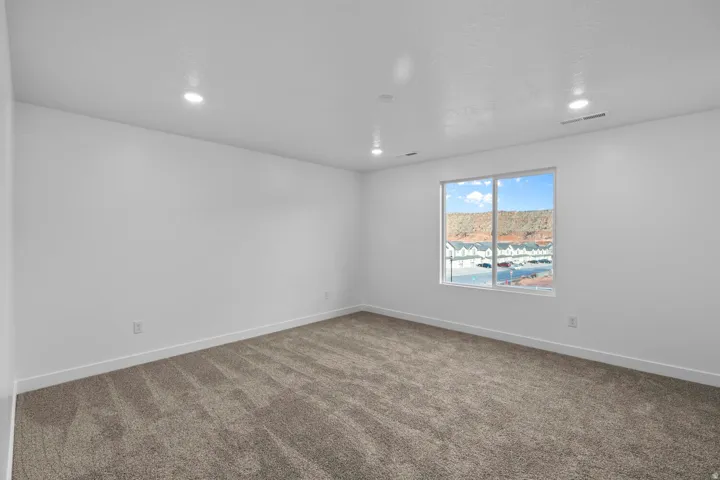 Recessed lighting throughout, neutral carpeting, expansive window, and crisp white walls