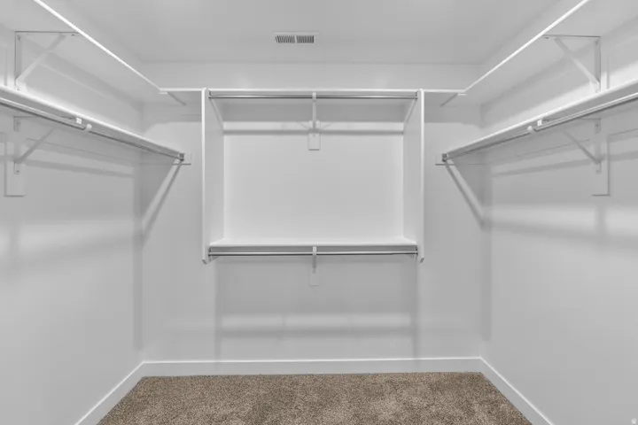 Spacious walk-in closet with multiple hanging rods, integrated shelving, and neutral carpeting