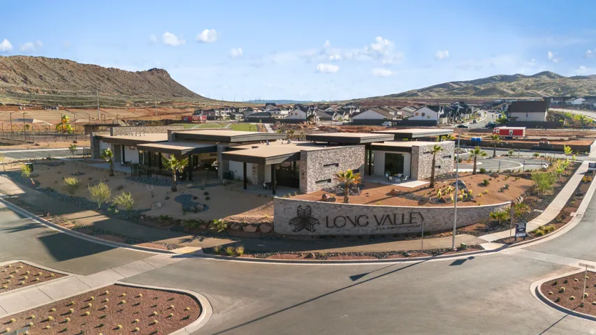 Community entrance with stone signage, modern architectural style, desert landscaping, and mountain backdrop