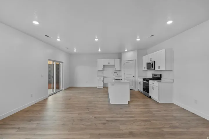 Open-concept living space featuring wood-finish flooring, recessed lighting, and a kitchen with white cabinetry and stainless steel appliances