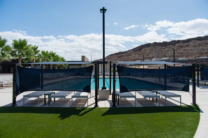 Swimming pool with surrounding shade structures, artificial turf, and palm trees