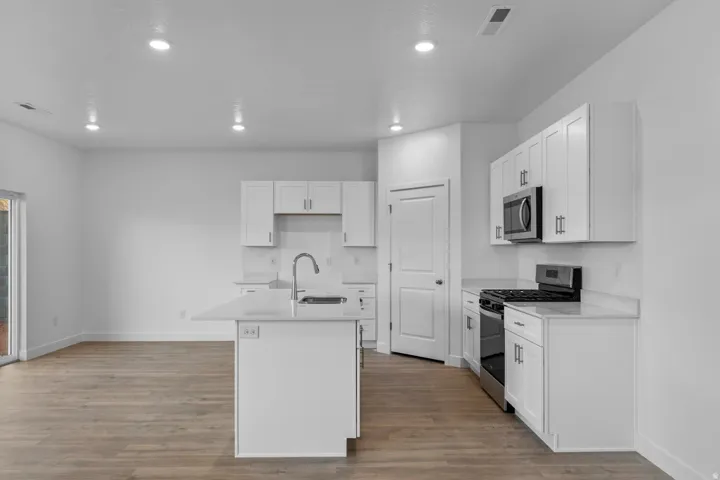 Kitchen featuring white shaker cabinetry, stainless steel appliances, a kitchen island with sink, recessed lighting, and wood-finish flooring