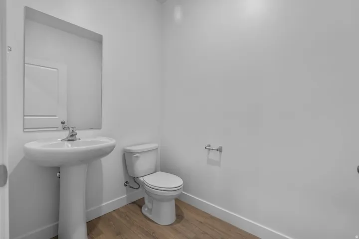 Pedestal sink with chrome faucet, wall-mounted mirror, white toilet, and wood-finish flooring