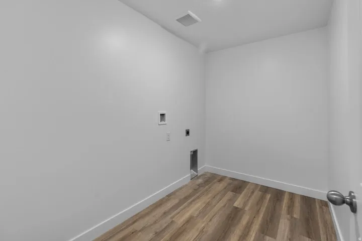 Dedicated laundry space with wood-finish flooring, white walls, and pre-installed utility connections