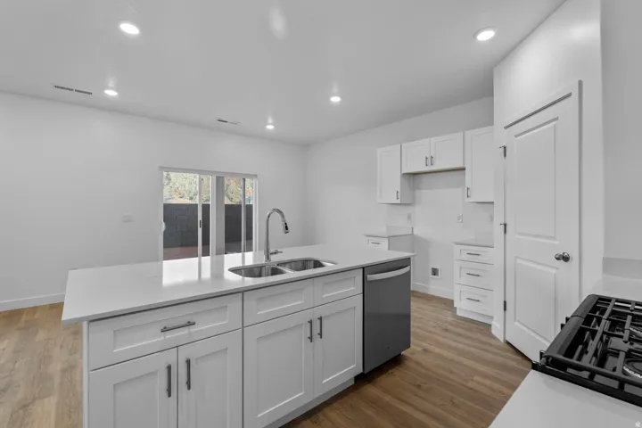 Kitchen featuring a center island, dual basin sink, wood-finish flooring, white cabinetry, and recessed lighting