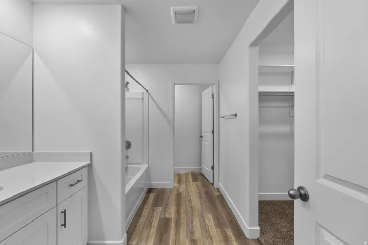 Bathroom featuring wood-finish flooring, a white vanity with a light-colored countertop, and a built-in shower and tub combination