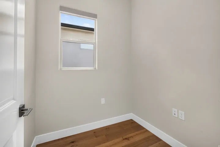 Wood-finish flooring with white trim, a single window with a roller shade, and a white interior door with dark hardware