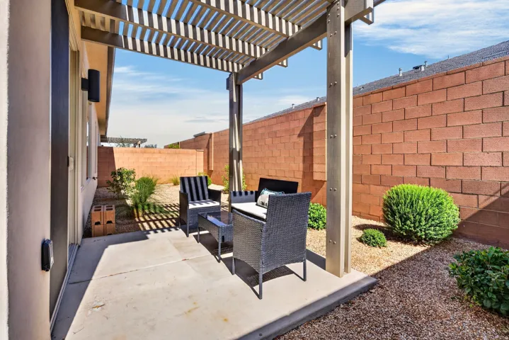 Covered patio area featuring a slatted pergola, concrete flooring, and decorative gravel landscaping