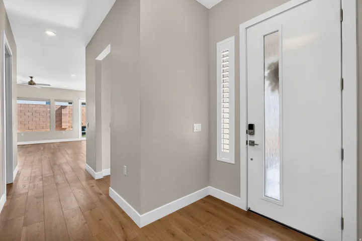 Entryway featuring a white door with frosted glass panel, an adjacent window with white plantation shutters, and wood-finish flooring extending into the interior