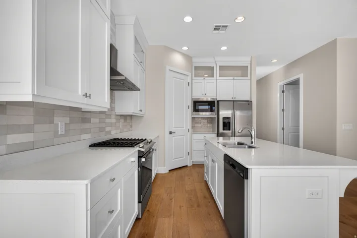 Kitchen featuring white shaker cabinetry, stainless steel appliances, solid surface countertops, a tile backsplash, and wood-finish flooring