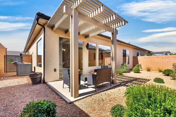Concrete patio featuring a slatted pergola, sliding glass door, stucco exterior, and gravel landscaping