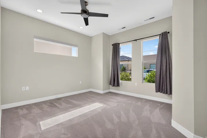 Bright secondary bedroom showcasing neutral wall finishes, plush carpet flooring, and abundant natural light from dual glass doors with thermal-lined drapery
