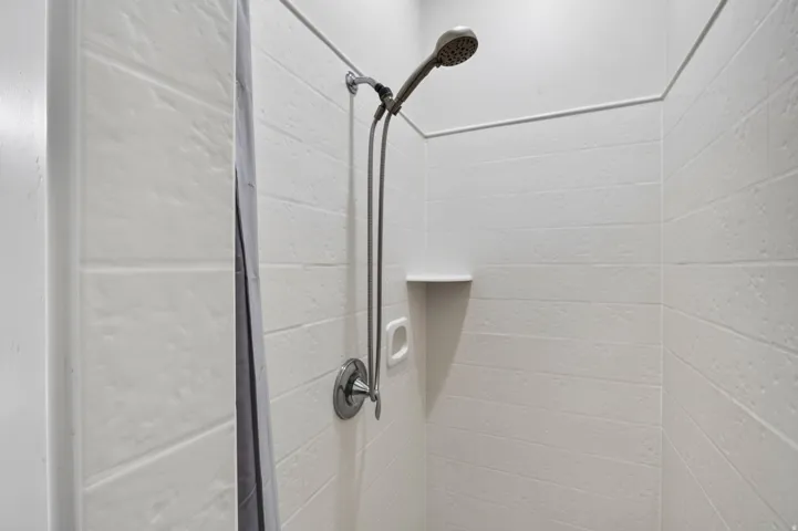 Shower enclosure with textured white subway tile, a built-in corner shelf, and a chrome shower fixture