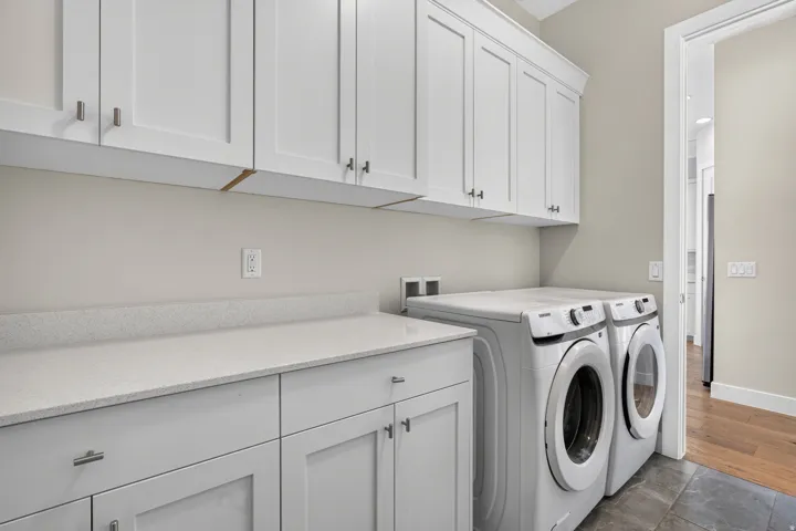 White shaker-style cabinetry with crown molding, light-toned countertops, and dark-toned flooring