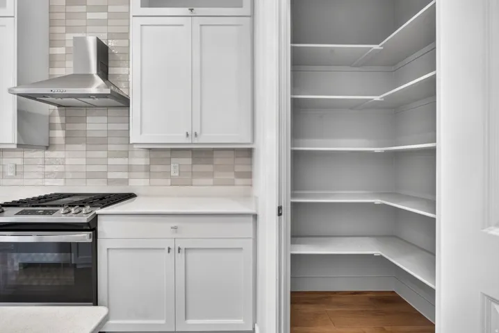 Well-appointed kitchen featuring a stainless steel range hood, white shaker-style cabinetry, and a subway tile backsplash