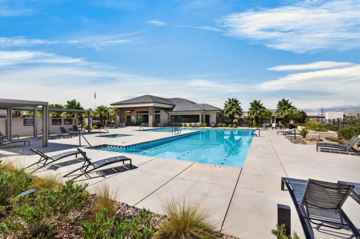 Resort-style pool with integrated spa, expansive concrete decking, covered lounging areas, and natural desert landscaping