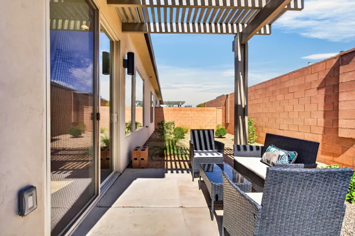 Expansive concrete patio with an attached louvered pergola, sliding glass door access, and exterior wall-mounted lighting