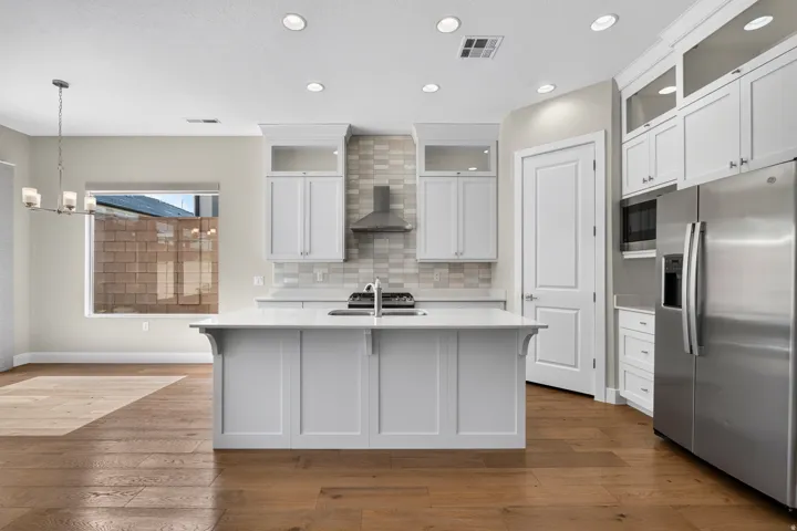 Kitchen with wood-finish flooring, white cabinetry, a central island with an integrated sink, stainless steel appliances, and recessed lighting