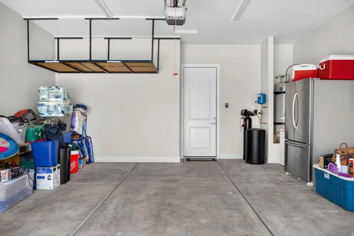 Concrete flooring with expansion joints, overhead storage racks, white paneled door, and ceiling-mounted lighting fixtures