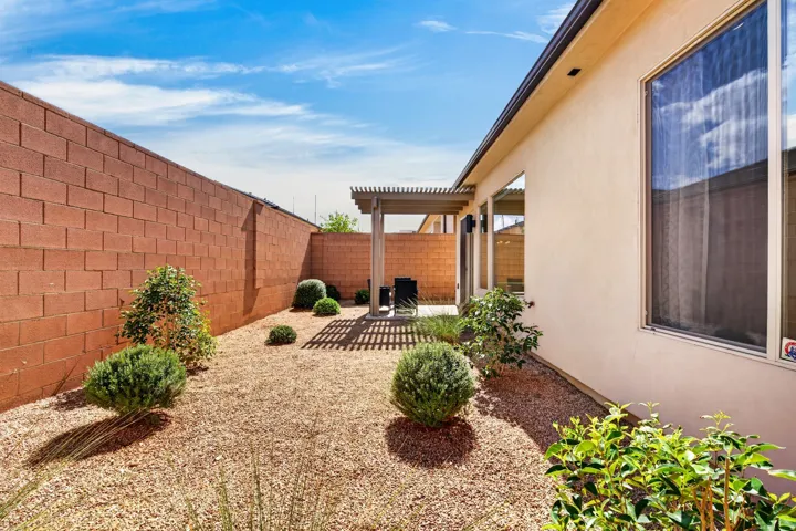 Private exterior featuring a covered patio, decorative rock landscaping, mature shrubs, and a block wall perimeter