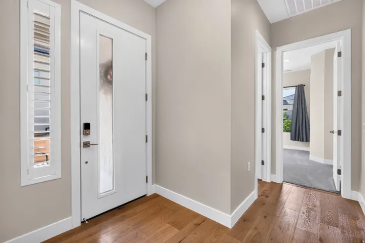 Hardwood-finish flooring, white entry door with frosted glass panel, and coordinating side panel with white plantation shutters