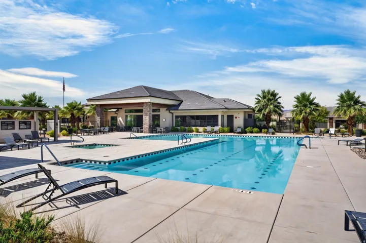 Expansive community pool with integrated hot tub, surrounded by a paved deck and mature palm trees