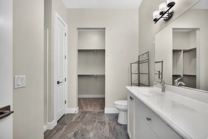 Vanity with integrated sink, expansive mirror, three-light fixture, tiled flooring, and built-in closet shelving