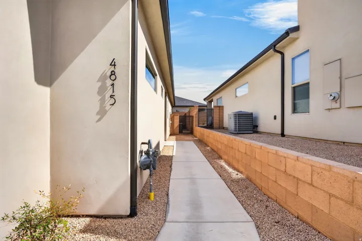 Stucco exterior with black house numbers, concrete walkway, gravel landscaping, and a retaining wall