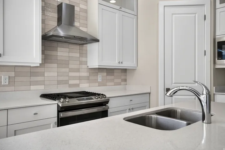 White shaker cabinetry, light-toned backsplash, stainless steel range with hood, dual basin stainless steel sink, and light-toned countertops
