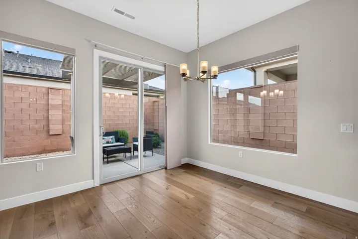 Spacious room featuring wood-finish flooring, a contemporary chandelier, two large windows, and a sliding glass door leading to a patio with a covered pergola