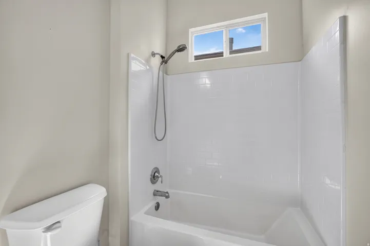 Bathtub and shower combination featuring white subway tile-patterned surround, brushed nickel fixtures, and transom window