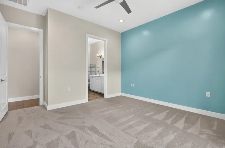 Wall-to-wall carpeting, recessed lighting, ceiling fan, and an open doorway leading to a bathroom with a vanity