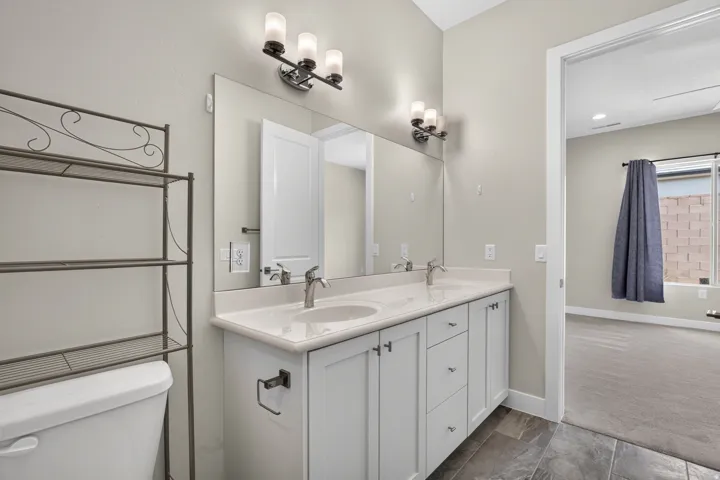 Double vanity with integrated sinks, white cabinetry, chrome fixtures, and a full-width mirror