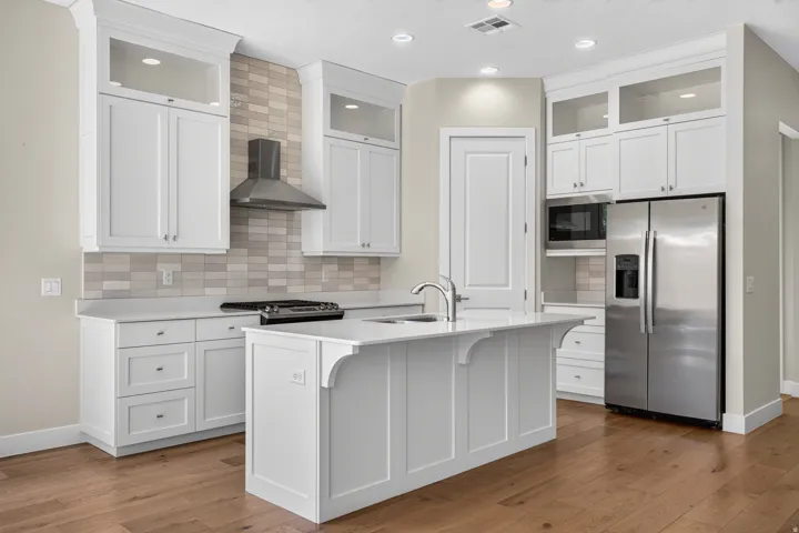 Gourmet kitchen with white shaker cabinetry, stainless steel appliances, a center island with a sink, quartz countertops, and wood-finish flooring