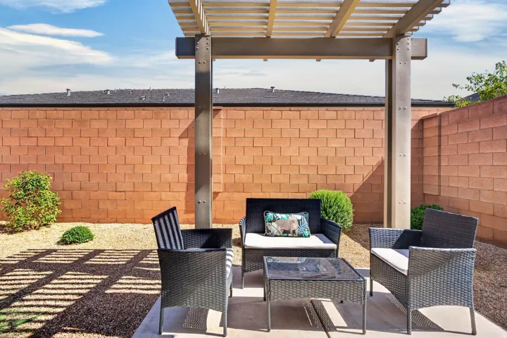 Outdoor patio with a slatted pergola, concrete flooring, gravel ground cover, and a block wall perimeter