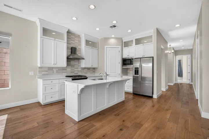 Kitchen featuring an island with an integrated sink, white cabinetry, stainless steel appliances, a tiled backsplash, and wood-finish flooring