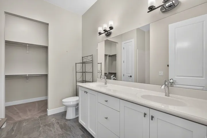 Dual vanity with integrated sinks, contemporary wall sconces, expansive wall mirror, white flat-panel cabinetry, and dark tile flooring