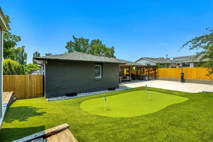 Putting green with artificial turf, wood pergola, concrete patio, dark brick exterior, and wooden privacy fencing