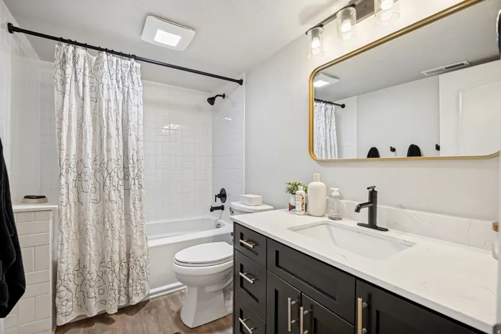 Wood-finish flooring with a white bathtub and tiled shower surround