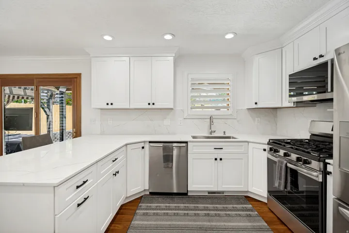 White shaker cabinetry, stainless steel appliances, white countertops, recessed lighting, and wood-finish flooring