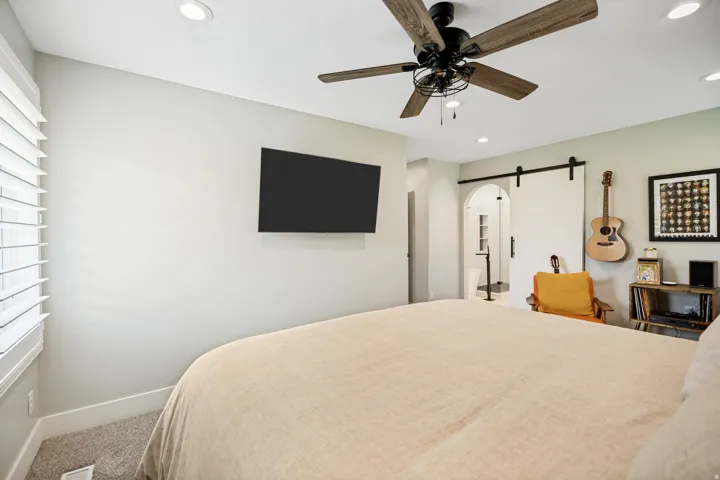 Recessed lighting, wood-finish ceiling fan, wall-mounted television, white plantation shutters, and a sliding barn door